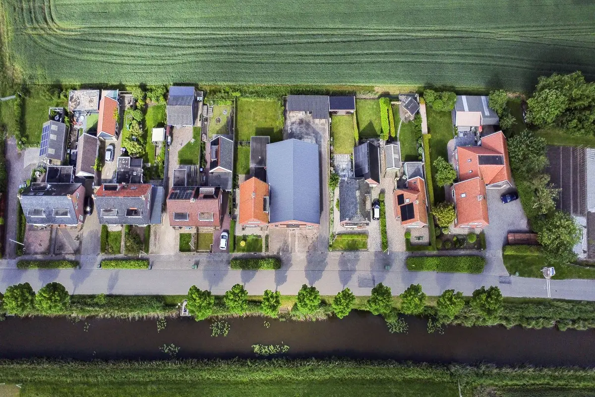 Luchtfoto van een rij woningen langs een vaart in het Friese land
