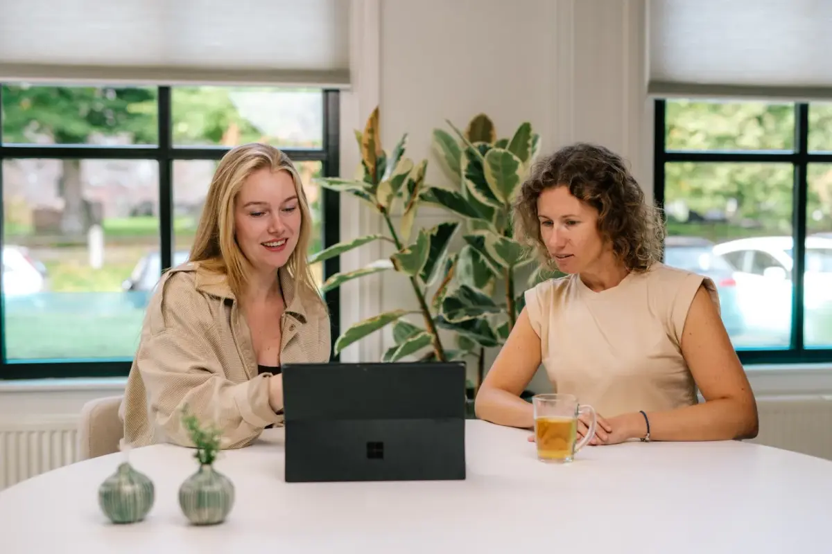 Twee vrouwen in gesprek aan een ronde tafel met een tablet