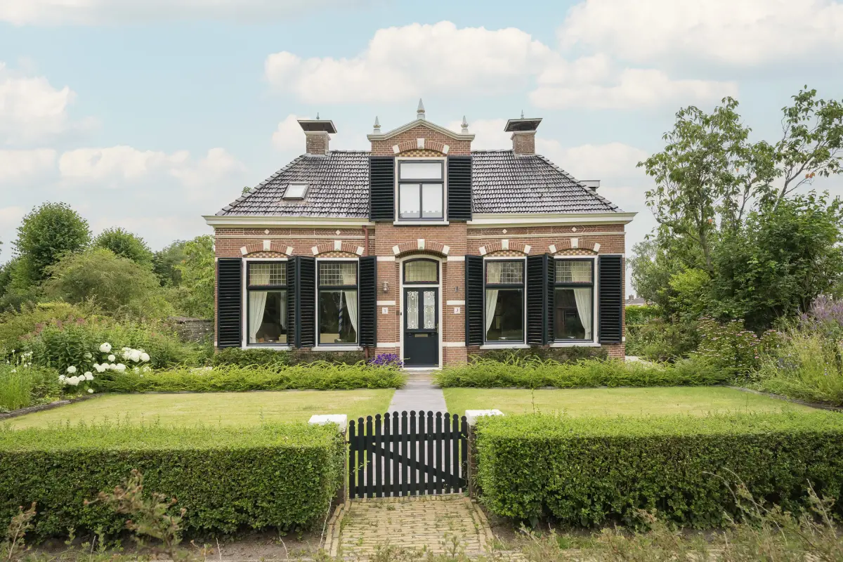Woning met zwarte luiken en een omheinde voortuin onder een bewolkte lucht